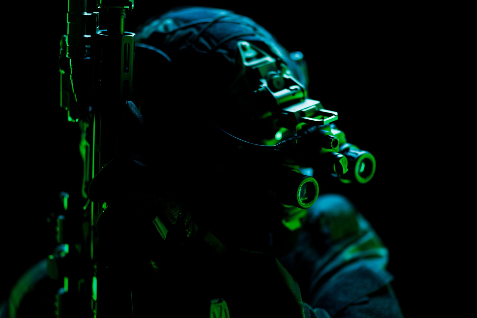 Silhouetted tactical figure in night vision equipment under green lighting
